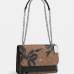 Cartera Coach Klare lazos negros vista tres cuartos con cadena plateada