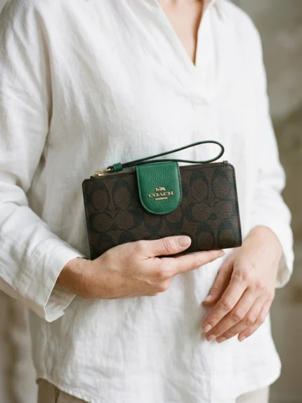 Coach monograma marrón con lengüeta verde y logo dorado — en la mano