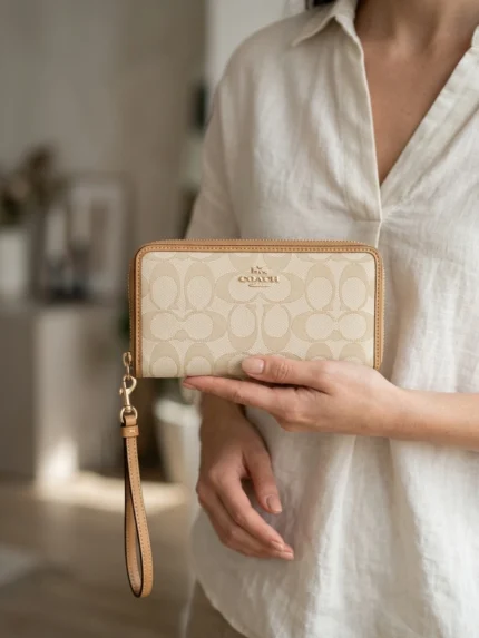 Coach monograma crema y borde camel, compacta con cierre y asa — en la mano