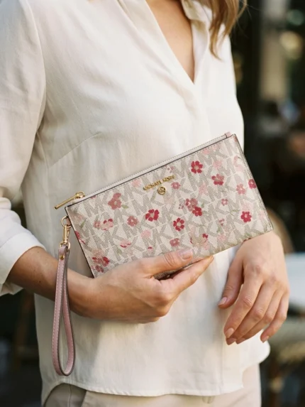 Michael Kors marfil con monograma y flores rosas, sobre plano con cierre y asa rosa — en la mano