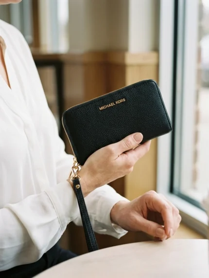 Michael Kors negra compacta con cierre perimetral y asa — en la mano